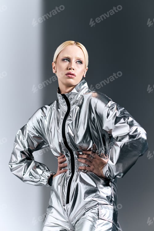 Preview: attractive blonde woman in robotic silver attire posing in motion and looking away on gray backdrop