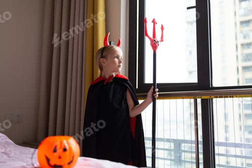 Preview: Little Girl in costume of devil with red horns at home. Happy Halloween concept