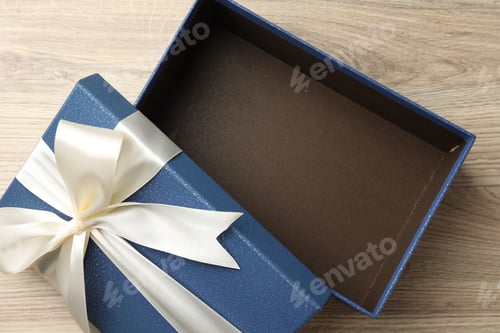 Preview: Opened gift box with beautiful lid on light wooden table, top view