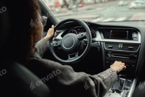 Preview: SIde view of businesswoman driving car with one hand on steering wheel and another on