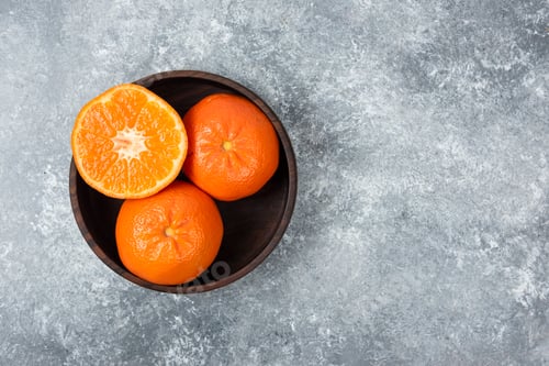 Preview: A wooden bowl full of juicy orange fruits on stone background