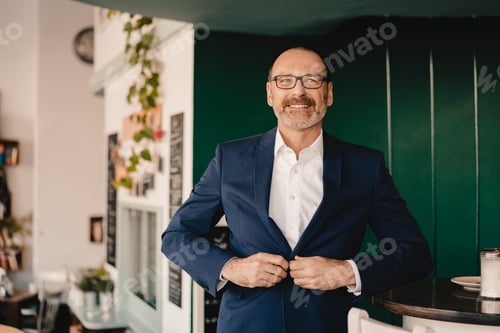 Preview: Confident mature businessman in a cafe buttoning his jacket