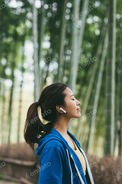 Preview: Young Asian woman using earphones outdoors