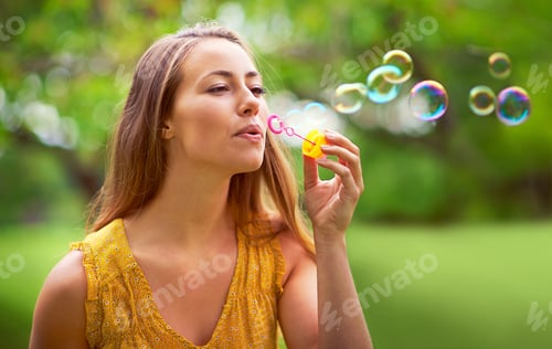 Preview: Feeling like a little girl again. Shot of a carefree young woman blowing bubbles in the park.