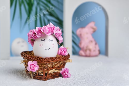 Visualização: Ovo de páscoa branco natural com rosto doce desenhado em grinaldas florais em uma cesta de vime no tropical