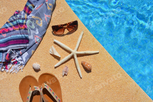 Preview: Summer flat lay. Sandals, sunglasses, starfish seashells and beach wrap on side of swimming pool