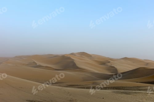Preview: Smooth sand dunes under a hazy sky in a vast desert landscape.