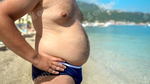 Preview: Young overweight man releasing his big fat belly on the sea beach. Concept of health, slimming