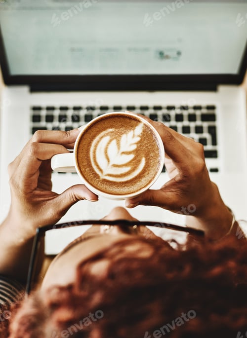 Preview: High angle shot of a young woman drinking coffee while working on a laptop in a cafe