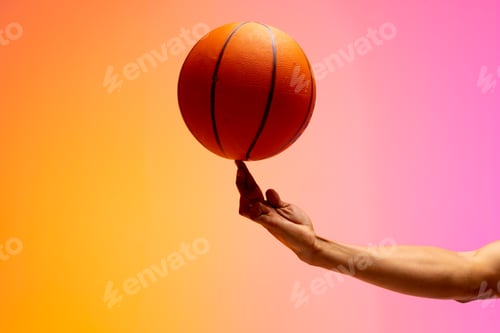 Preview: Image of hand of biracial basketball player spinning basketball on pink to orange background