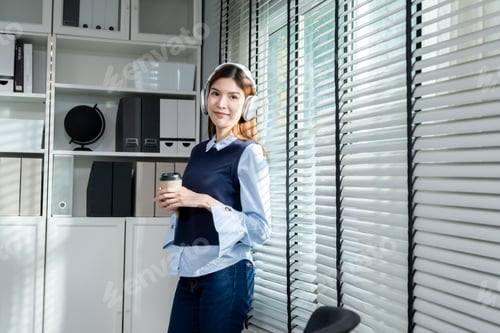 Preview: Asian businesswoman listen to podcast with headphones in the office.