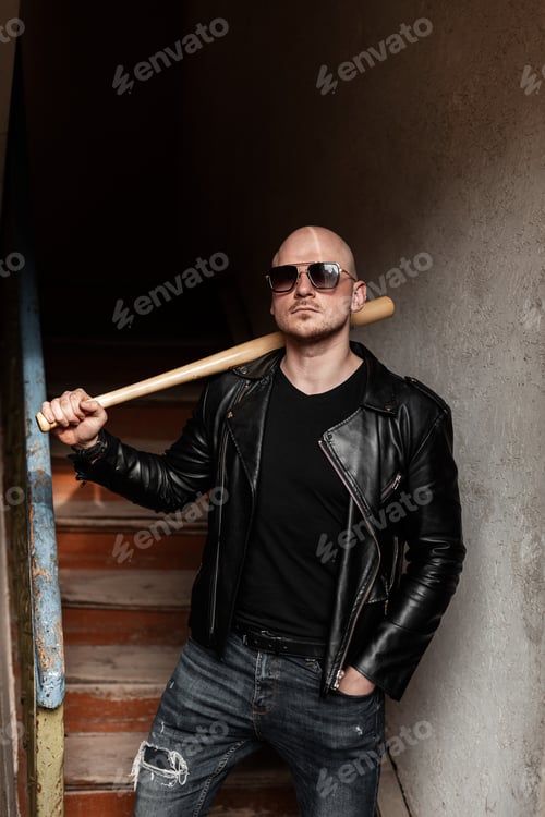 Preview: Brutal bald man in fashion sunglasses in black vintage leather jacket in jeans with baseball