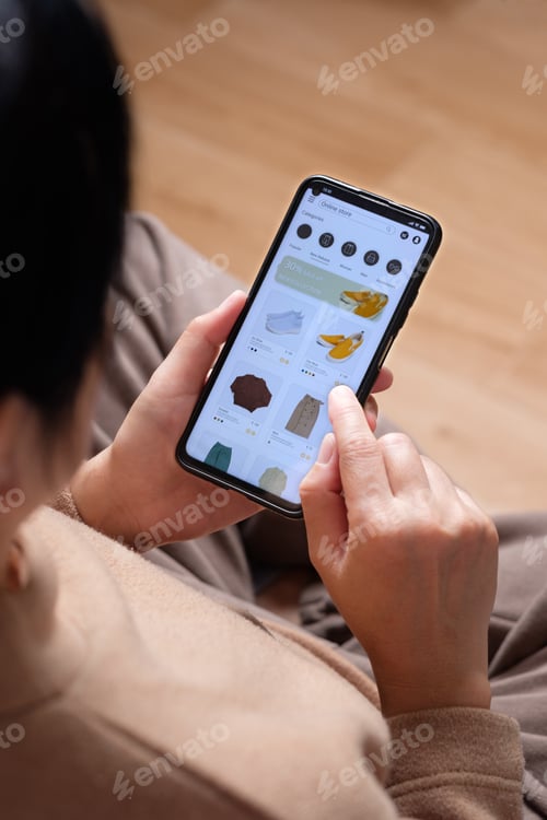 Preview: close up hand browsing shopping fashion mobile app on sofa at home