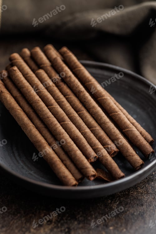Preview: Chocolate Wafer Rolls on plate on dark table.
