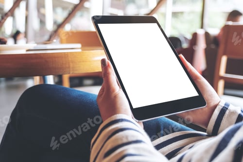 Preview: A woman holding black tablet pc with blank white desktop screen while sitting in cafe