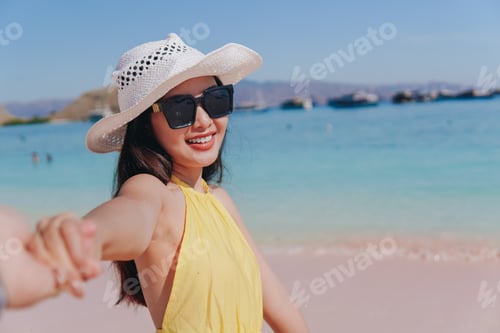 Smiling young Asian woman is holding hands with a man on Pink Beach, Labuan Bajo.