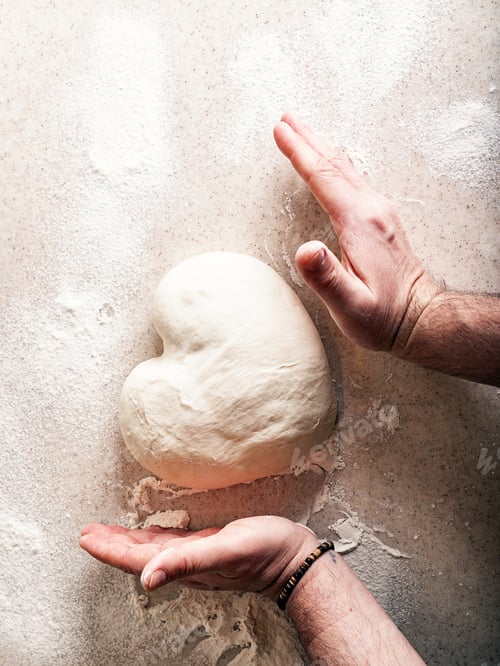 Preview: Male hands knead the dough in the shape of a heart. Human hands prepare dough for home baking