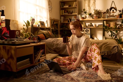 Preview: Young Woman Sitting on Floor Using Laptop and Drinking Coffee
