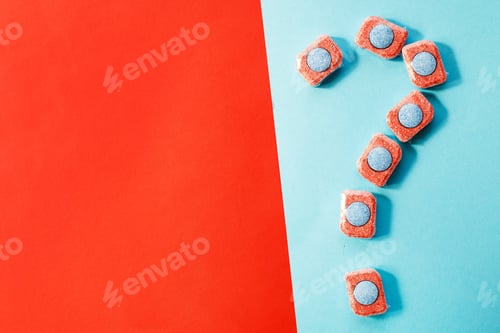 Preview: capsules for kitchen dishwashers and a question mark on a blue and red background. flat lay.