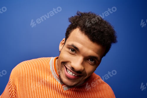Preview: Handsome man smiling brightly against a vibrant blue background in a casual portrait setting
