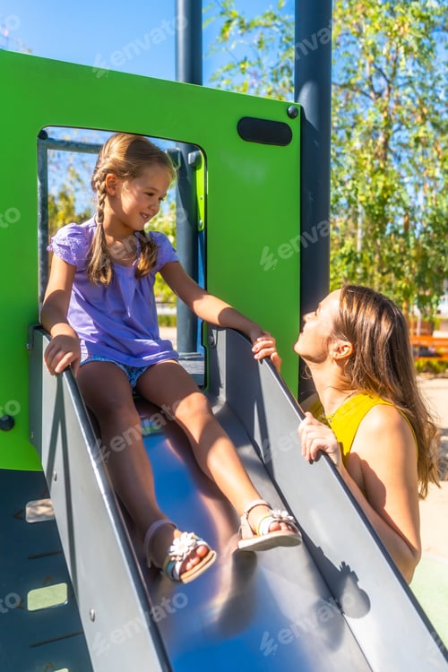 Preview: Mother and daughter playing on playground slide outdoors