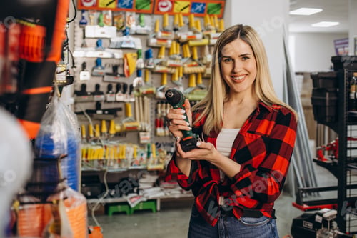 Preview: Young woman choosing electric screwdriver in hardware store. Side view of pretty lady examining