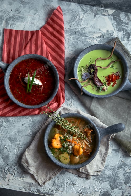 Preview: Gray plates with different soups on a gray background. Plate with asparagus soup with octopus, a