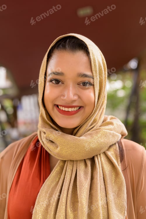 Preview: Face of happy young beautiful Indian Muslim woman smiling in the city with nature