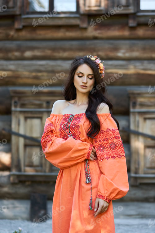Preview: Beautiful Slavic woman in an orange ethnic dress and a wreath of flowers on her head. Beautiful