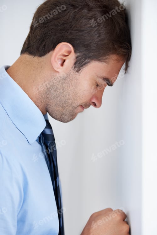 Preview: Profile of a businessman standing with his forehead against the wall and his fist punching the wall