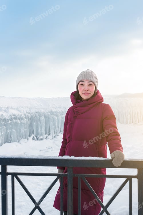 Preview: Smiling enchanting asian woman in front of frozen ice of sea waves at sunny winter day