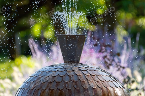 Preview: Water fountain sprays mist in a garden filled with colorful flowers during sunny afternoon