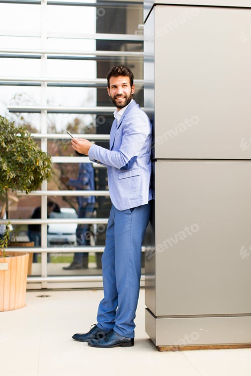 Preview: Young man with mobile phone by office building