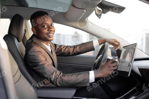 Preview: Happy smiling African American male driver sitting behind the self-driving steering wheel of an
