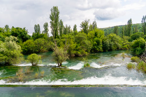 Preview: Serene krka waterfall flow amid lush greenery on a cloudy day, Croatia