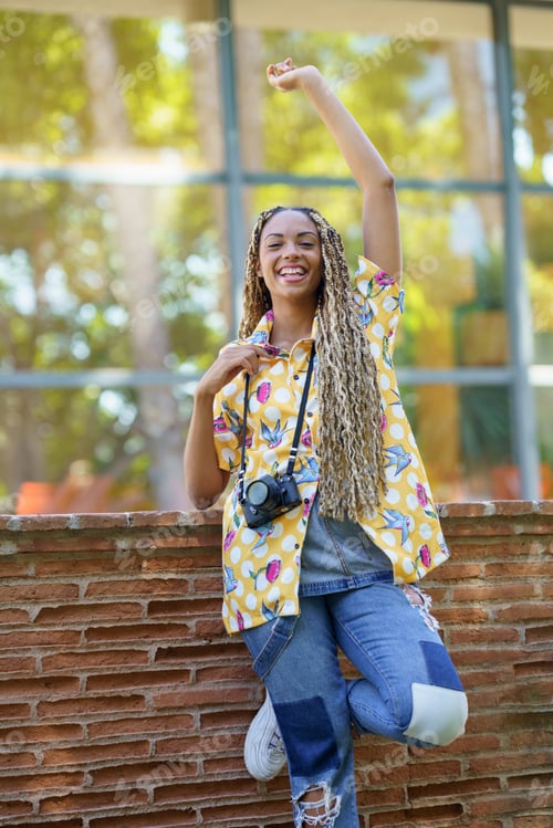 Preview: Black woman with African braids, raising her arm in joy. Girl holding a camera.