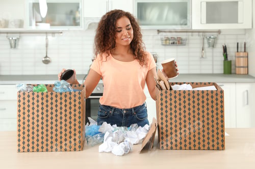 Preview: Young African-American woman sorting garbage in kitchen. Recycling concept