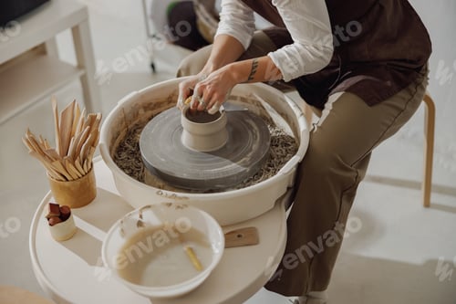 Preview: Female potter in apron making shape of clay vase on spinning pottery tool in ceramic workshop
