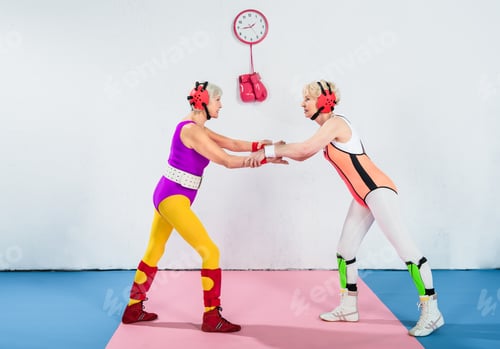 Preview: side view of senior female wrestlers in head protection fighting and looking at each other