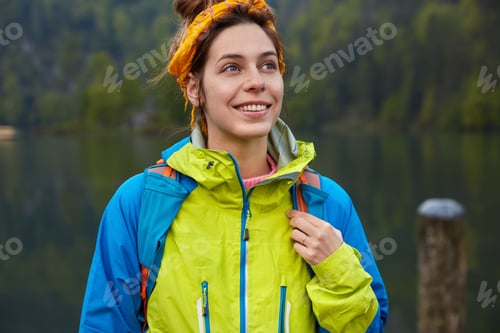 Preview: Dreamy positive female traveler has active recreation, poses on green forest and lake, wears casual