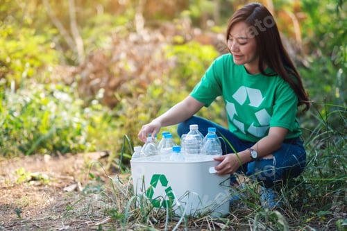 Preview: A beautiful asian woman collecting garbage plastic bottles into a recycle bin in the outdoors