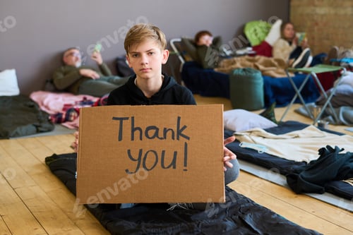 Preview: Grateful boy in casualwear holding cardboard poster while sitting on the floor