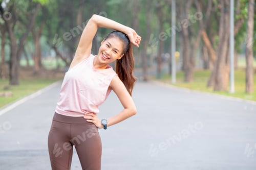 Preview: Asian woman stand and do right arm stretching also look at camera and smile in park