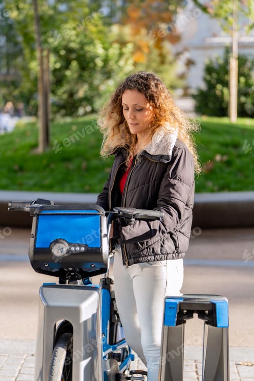 Vorschau: Junge Frau entsperrt ein gemeinsames Elektrofahrrad in urbaner Umgebung