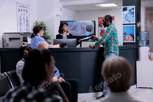 Preview: African american patient handing clipboard with completed form to hospital receptionist