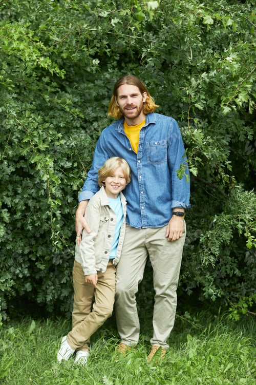 Preview: Portrait of happy father and son standing against greenery in park