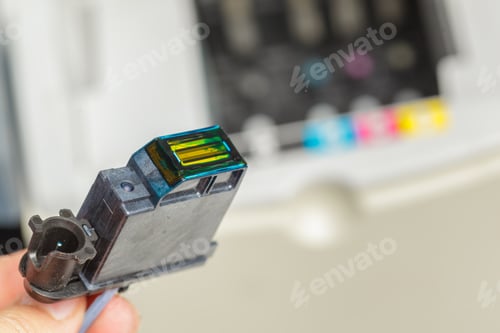 Preview: Color ink cartridge held by a person above a printer showing various colors
