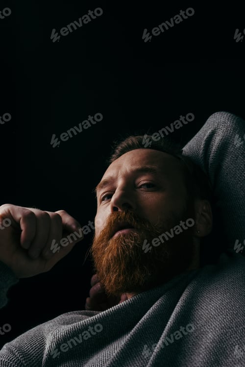 Preview: Low angle view of stylish bearded man in jumper looking at camera isolated on black with shadow