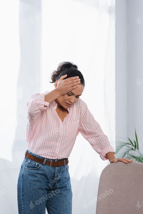 Preview: african american woman suffering from headache and leaning on sofa
