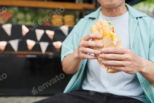 Preview: Close-up of young hungry man in casualwear holding appetizing hotdog